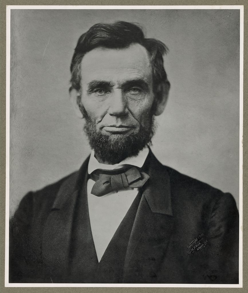 Abraham Lincoln wearing a suit and tie, he has a beard with no mustache.
