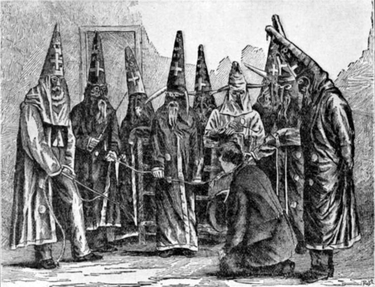 men in robes and cone-shaped hats circled around a man kneeling on the ground.