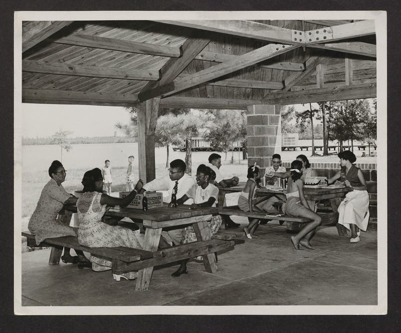 A family picnicking under a picnic shelter at Jones Lake State Park, circa 1950.