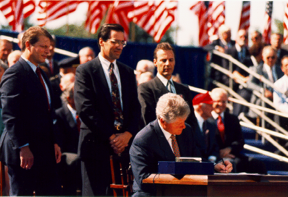 Clinton Signing NAFTA. He is seated outdoors at a table flanked by other men.