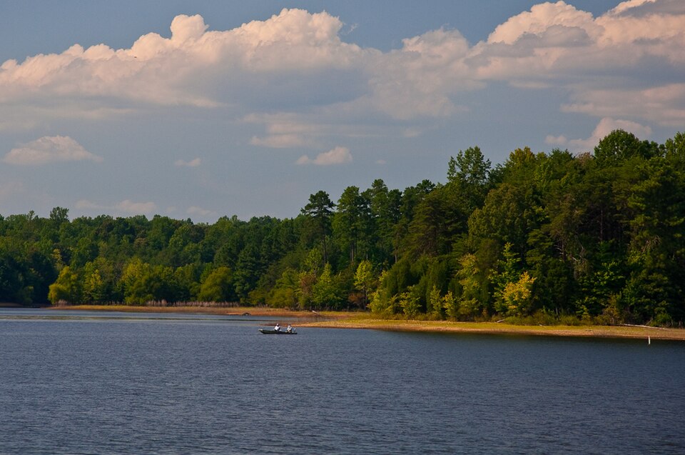 A lake with a boat on it. Trees line the shore.