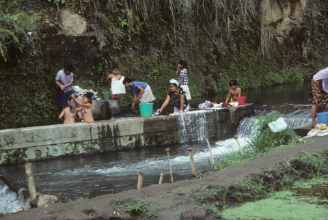 Family members bathe and do laundry at stream embankment