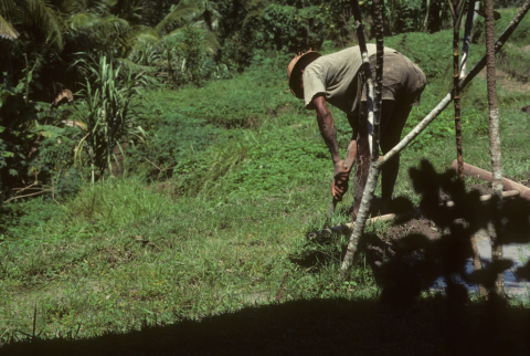 Farmer leans over and washes his feet after long day working wet-rice fields