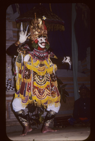 Masked male dancer holds up hands with long fingernails