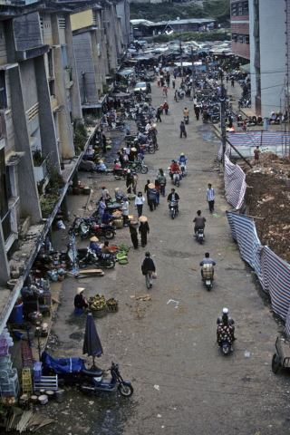 Elevated view of vendors, pedestrians, and motorcycles at urban market in Dalat