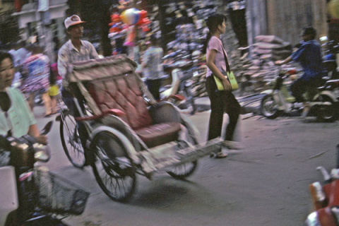 Front view of empty bicycle rickshaw driven in Hanoi and shoppers in motion