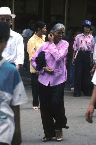 Woman with grey hair, black pants, and pink jacket crosses a busy Hanoi street