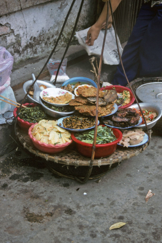 Hanging tray with stacked bowls of prepared foods sold by street vendor in Hanoi