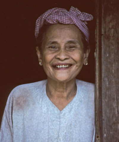 Smiling older woman wearing wrapped headcloth in doorway near Mytho