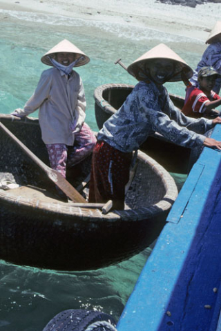 Two women with conical sunhats stand in round boat near Nha Trang