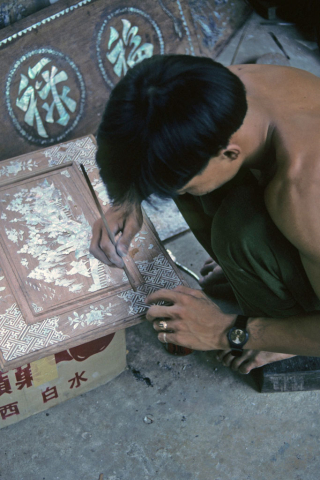 Man applies inlay designs to a wood plaque at handicraft workshop in Hoi An