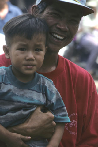 Laughing man in red T-shirt holds small boy in Ho Chi Minh City