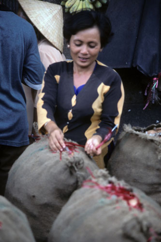 Woman sewing shut large sacks of produce in Ho Chi Minh City